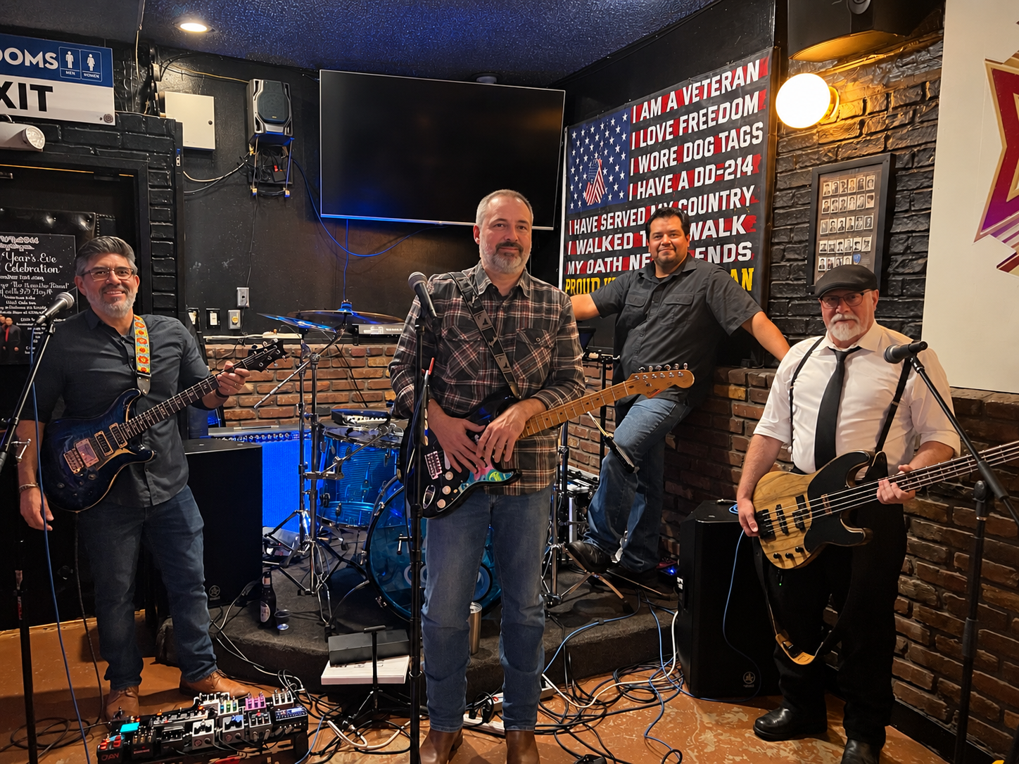 The four members of Black Hat Company with guitars, bass, and drums at a live venue